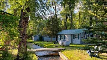 A rustic cabin with a stone stream, surrounded by lush greenery and trees.