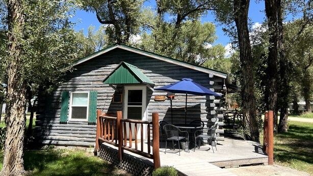 A rustic log cabin with a porch, a small deck, and outdoor seating.
