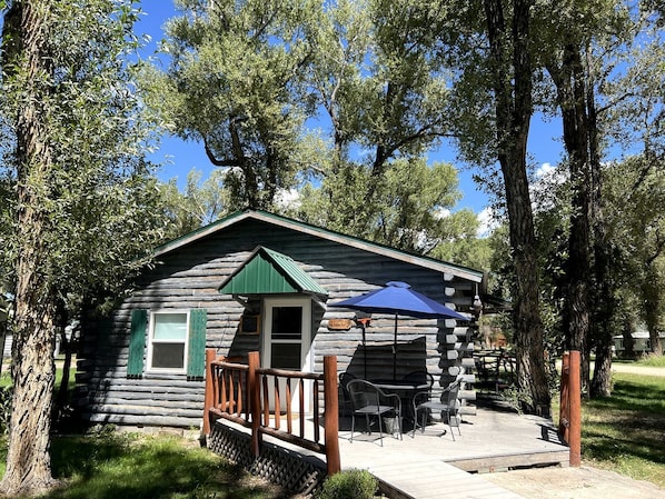 A rustic log cabin with a porch, a small deck, and outdoor seating.