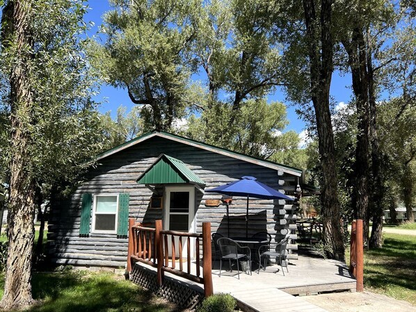A rustic log cabin with a porch, a small deck, and outdoor seating.