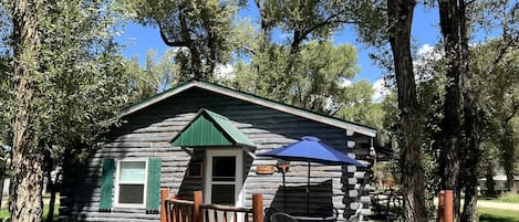 A rustic log cabin with a porch, a small deck, and outdoor seating.