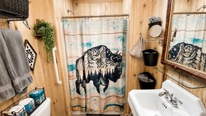 A wooden cabin bathroom with a toilet, sink, shower curtain, and a mirror.