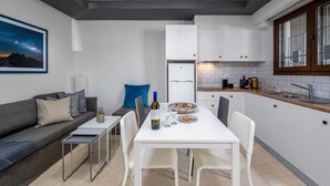 A compact living space with a kitchenette, a dining area with a table and chairs, a sofa, and a framed picture on the wall. - Rodini Anassa | Dimitra, Apartment (Rodos)