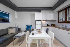 A compact living space with a kitchenette, a dining area with a table and chairs, a sofa, and a framed picture on the wall. - Rodini Anassa | Dimitra, Apartment (Rodos)