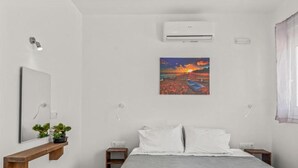 A bedroom with a bed, a nightstand, a wall-mounted air conditioner, a painting, and a mirror. - Summer Paradise Stegna (RODOS)