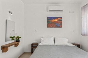 A bedroom with a bed, a nightstand, a wall-mounted air conditioner, a painting, and a mirror. - Summer Paradise Stegna (RODOS)