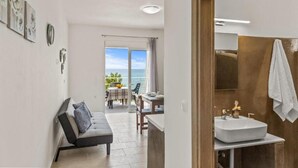 A modern bathroom with a sink and mirror, a sofa with cushions, and a view of the sea through the balcony. - Summer Paradise Stegna (RODOS)