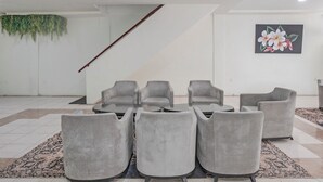Zona d'estar moderna amb cadires tapissades de gris disposades al voltant d'una taula central, una escala amb barana vermella i un quadre floral a la paret.
