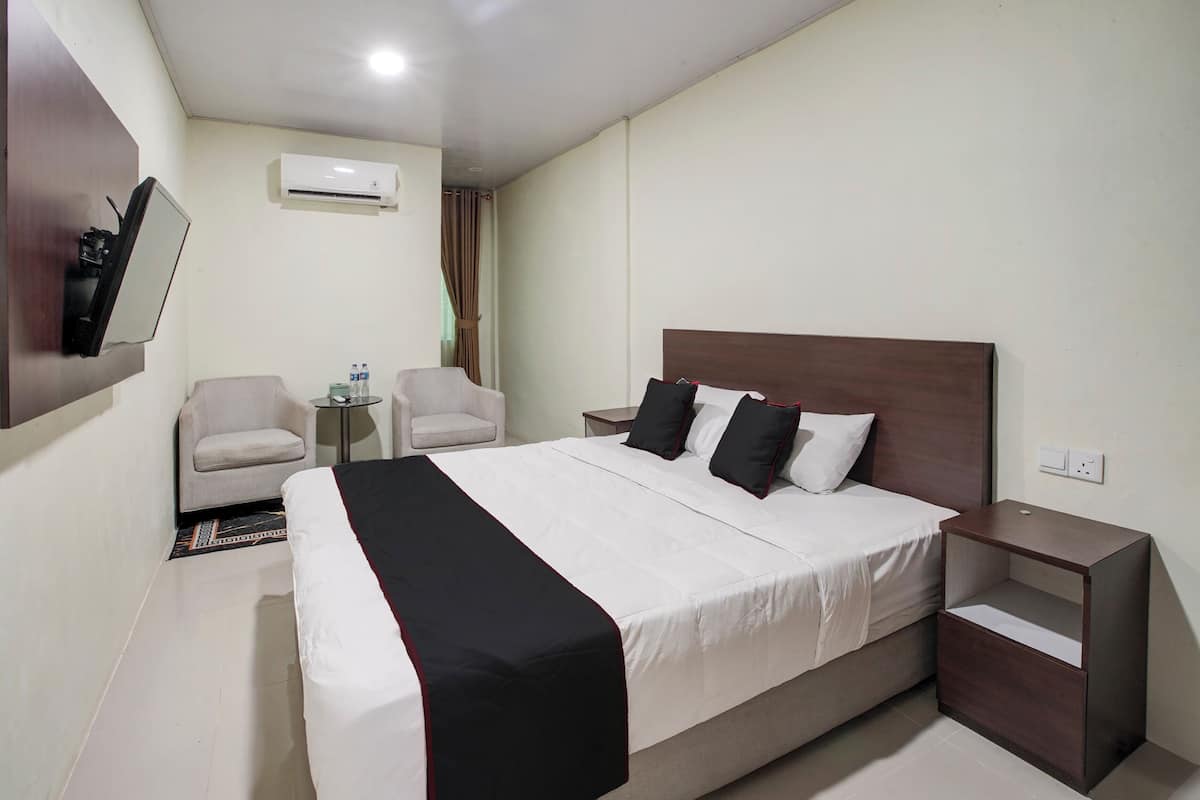 A hotel room with a large bed, two armchairs, a small table, and a nightstand.