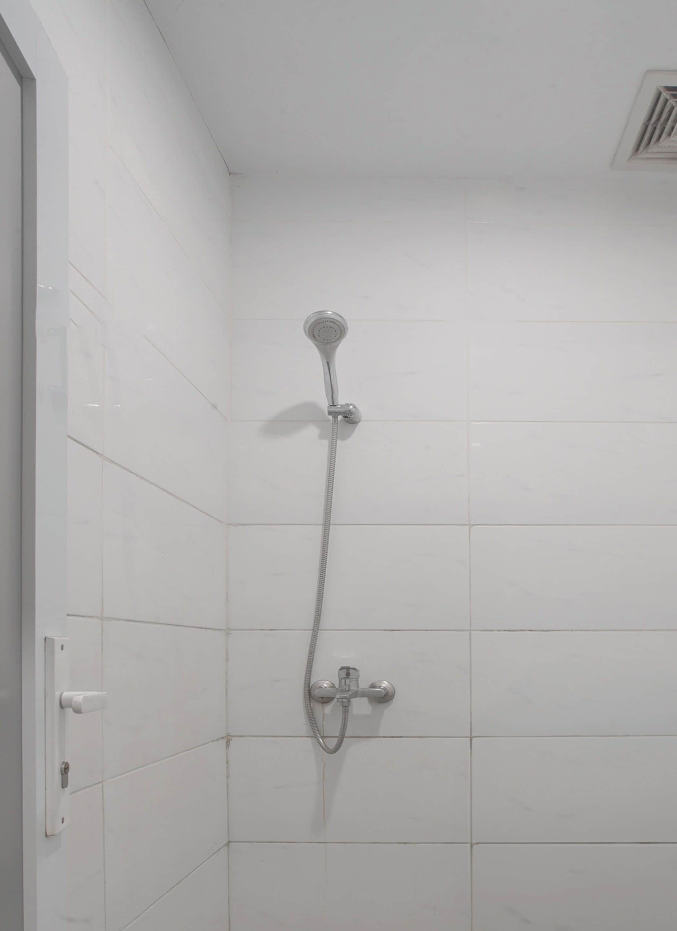 A shower with a handheld showerhead and a wall-mounted faucet in a tiled bathroom.