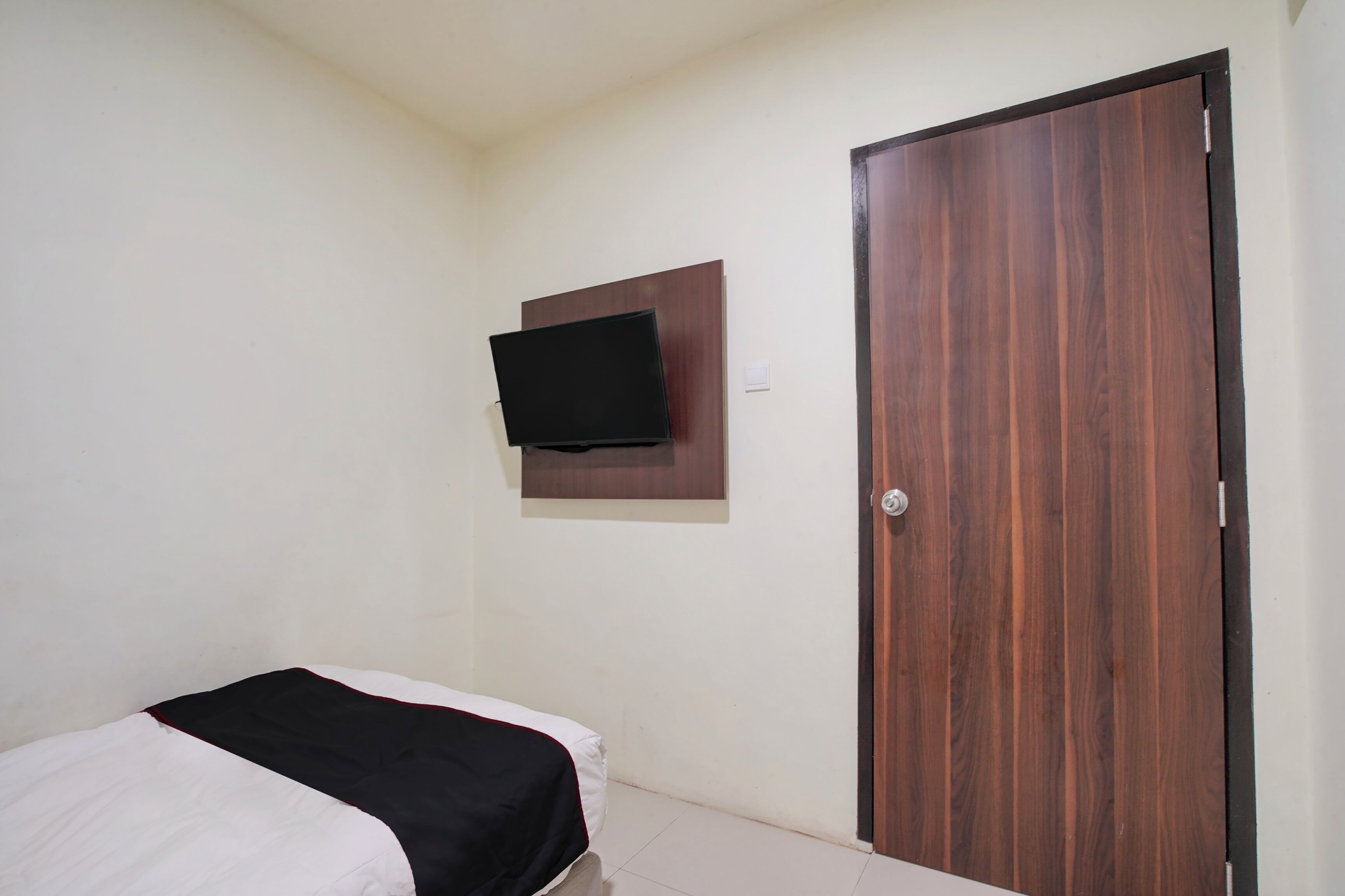Une chambre à coucher avec un lit, un téléviseur fixé au mur et une porte en bois.