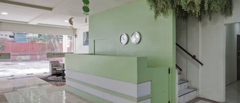 A reception area with a green counter, two clocks, a staircase, and a view of the outside.