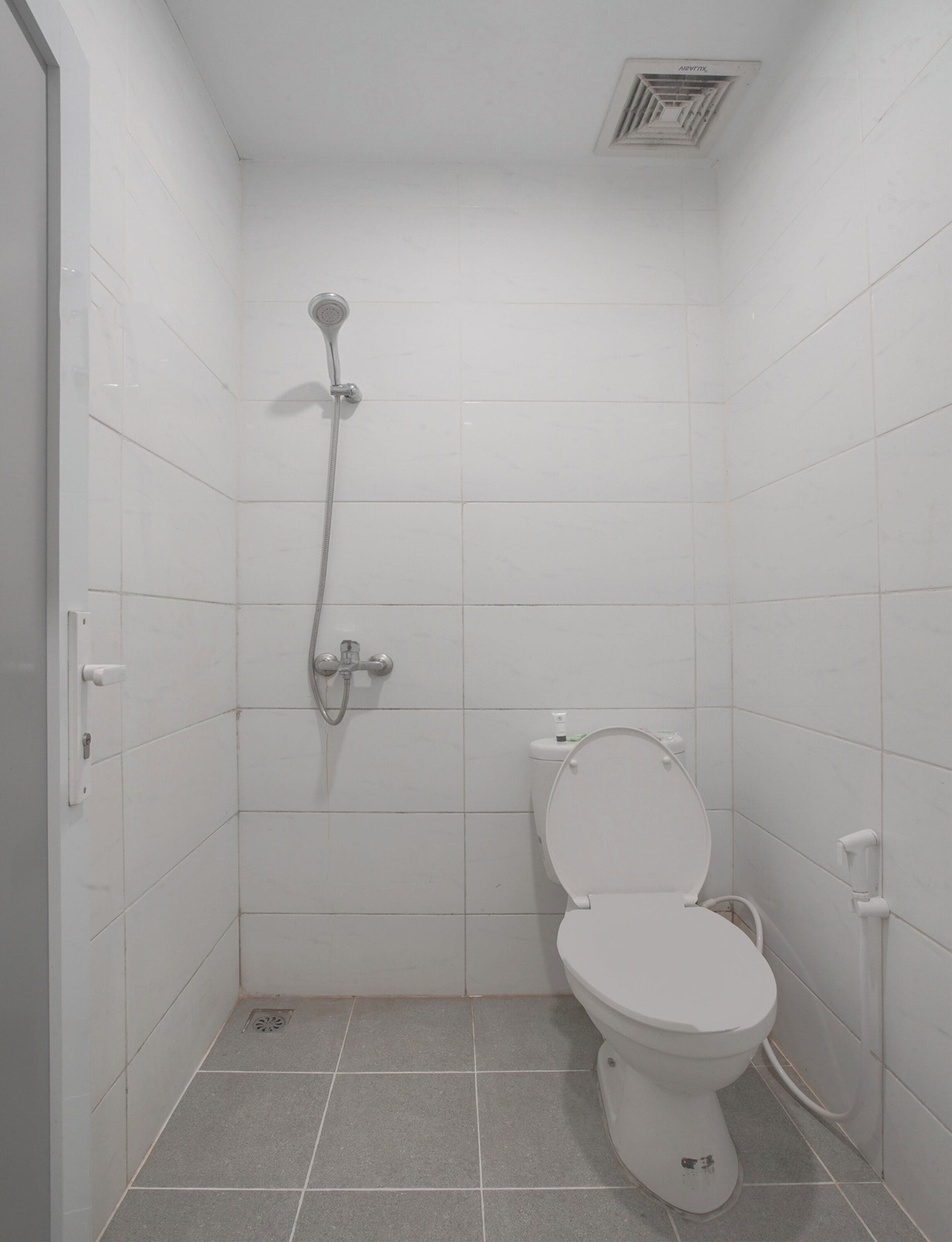 A small, white-walled bathroom with a toilet and a shower.
