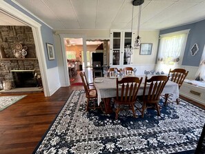 A dining room with a table set for four, surrounded by wooden chairs, a patterned rug, and a stone fireplace. - Incredible Cottage with Hot-tub in Penn Yan, New York (Penn Yan)