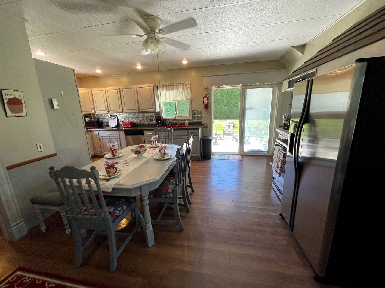 A kitchen with a dining table, chairs, a refrigerator, and a ceiling fan.
