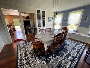 A dining area with a table set for four, surrounded by wooden chairs, a patterned rug, and a view of the kitchen and dining room through an open doorway. - Incredible Cottage with Hot-tub in Penn Yan, New York (Penn Yan)