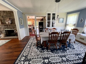 A dining room with a table set for four, surrounded by wooden chairs, a patterned rug, and a stone fireplace. - Incredible Cottage with Hot-tub in Penn Yan, New York (Penn Yan)
