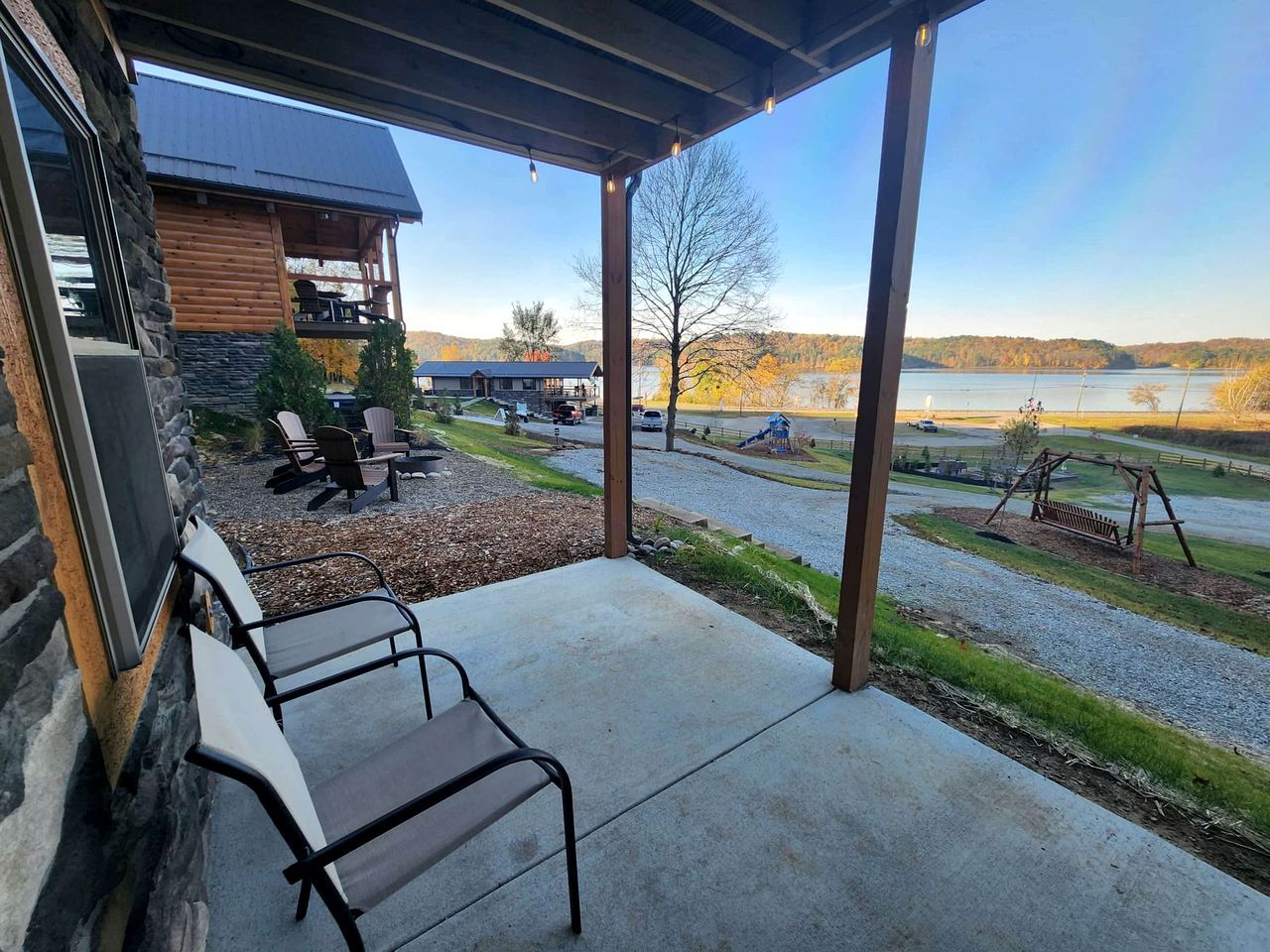 A covered patio with outdoor seating, a view of a lake, and a playground.