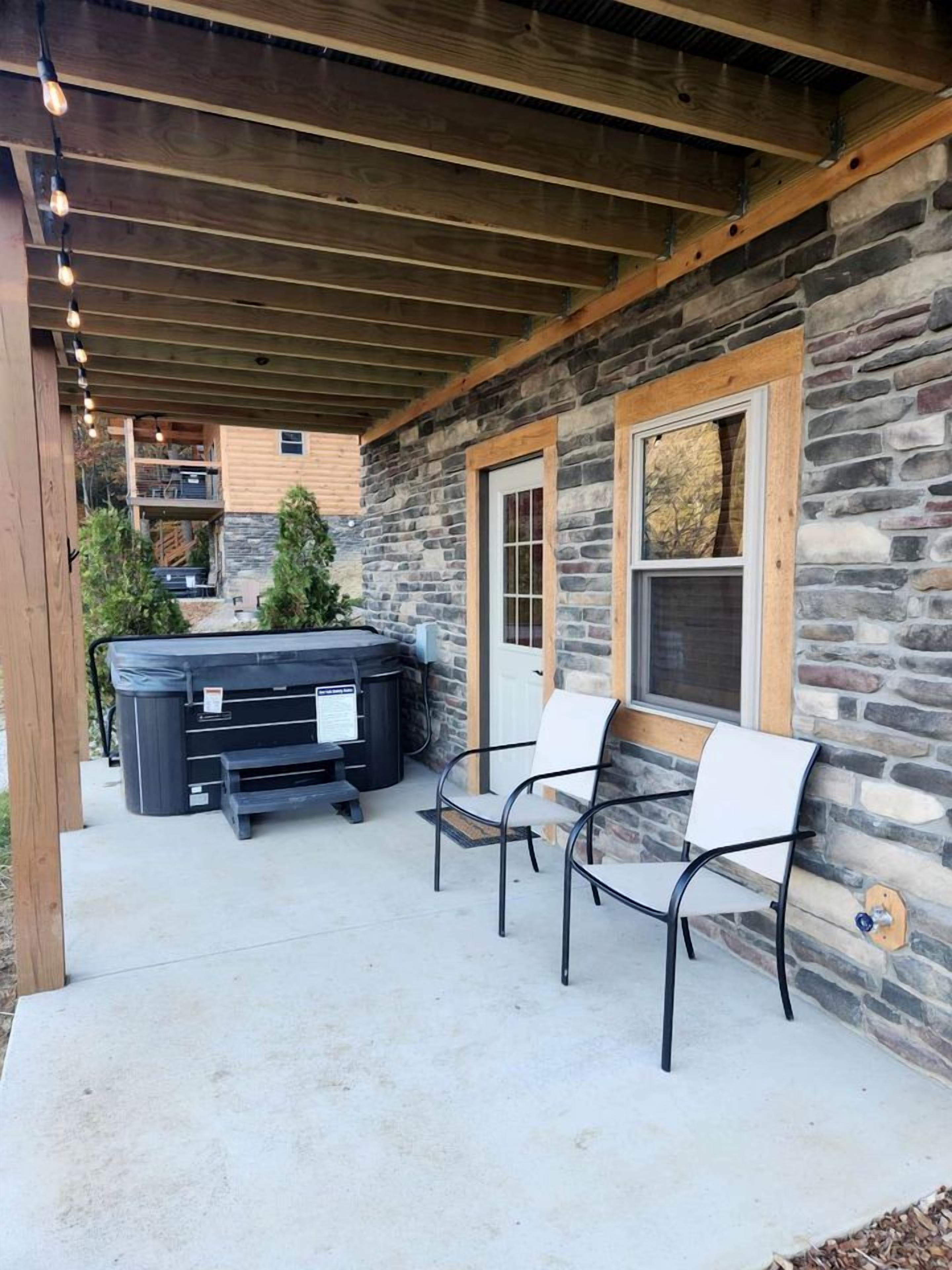 A stone building with a covered patio, outdoor seating, and a hot tub.