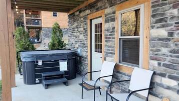 A stone building with a covered patio, outdoor seating, and a hot tub.