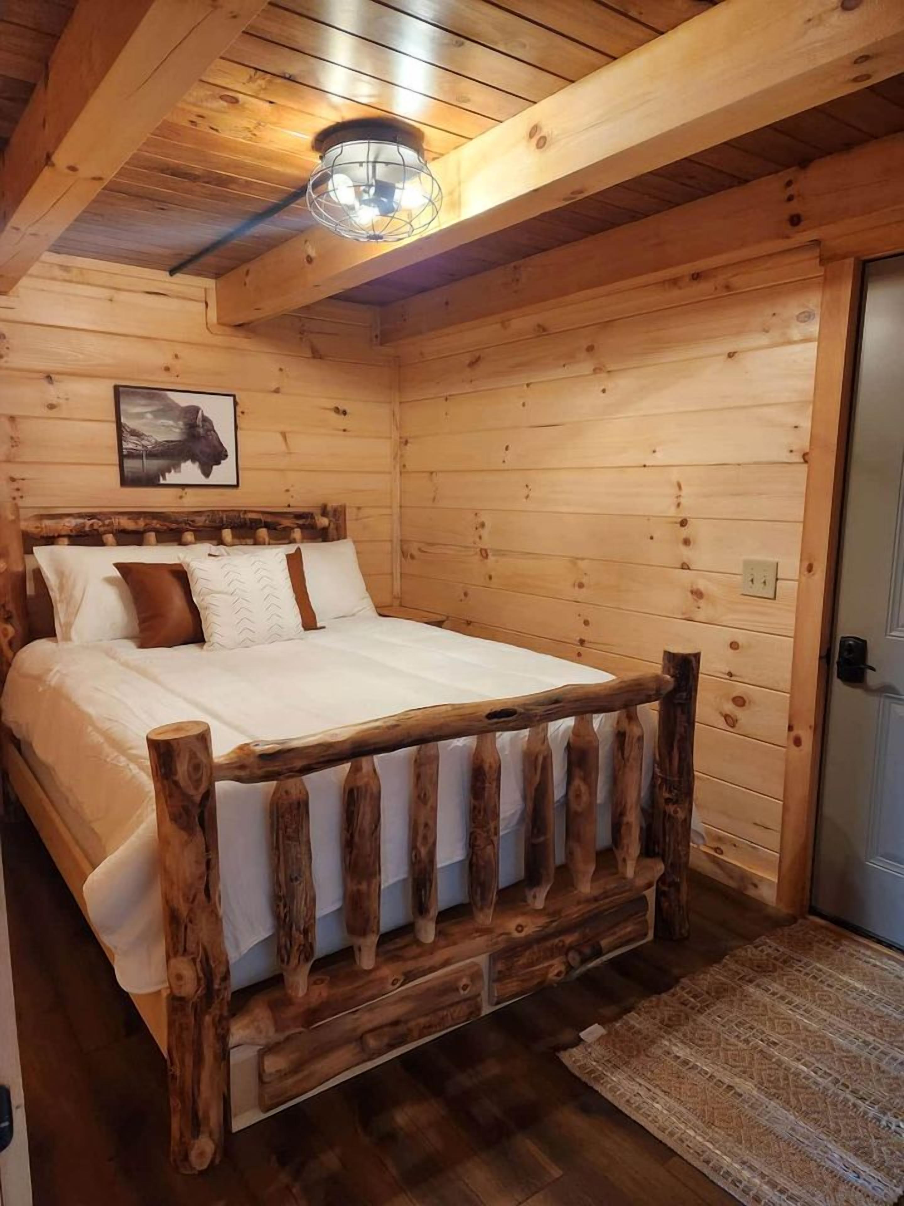 Un dormitorio de cabaña de madera con cama, cabecera de madera y lámpara en el techo.