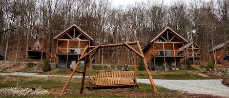 A wooden cabin with a swing set in front, surrounded by trees.