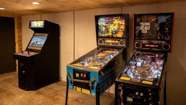 Una habitación con tres máquinas de pinball, techo de madera y paredes blancas.