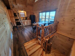 Innenansicht einer Holzhütte mit Treppe, Küche, Essbereich und einem großen Fenster mit Blick.