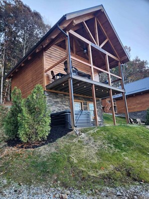 A two-story log cabin with a stone foundation, a covered porch, and a garage. - Group Friendly Cabin with Spa on the Deck near Tappan Lake in Ohio (Deersville)