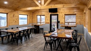 Una cabaña de madera con comedor, ventanas amplias y vista al lago.