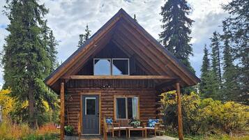 Una cabana de fusta amb un porxo, una zona de dinar i una finestra gran.