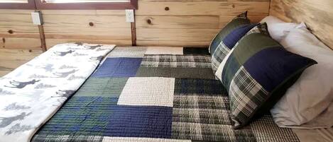 A wooden cabin interior with a bed featuring a patchwork quilt and plaid pillows.