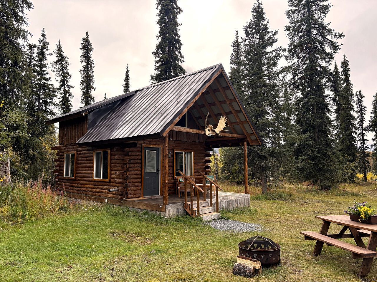 A rustic log cabin with a porch, a fireplace, and a picnic table.