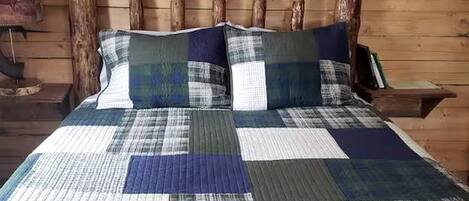 A bed with a quilt, wooden headboard, and a wall with a wooden log.
