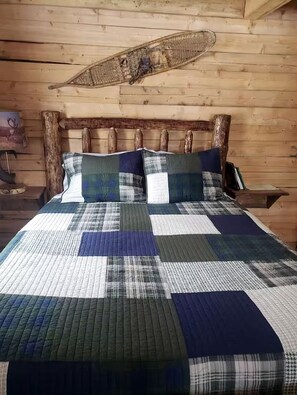 Una cama con colcha, cabecera de madera y una pared de troncos.
