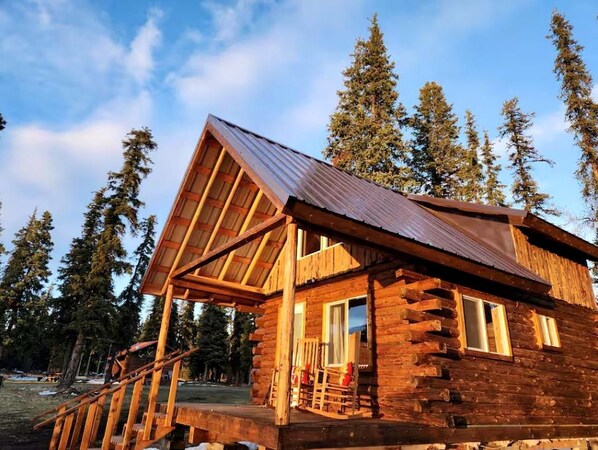 A log cabin with a porch, a covered deck, and a mountain backdrop.