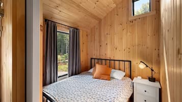 Een slaapkamer met houten lambrisering, een bed, gordijnen, een nachtkastje en een raam.
