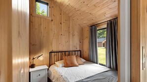 Camera da letto con rivestimento in legno, un letto, un comodino, una lampada e vista sull'esterno.