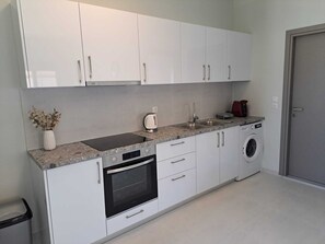 A modern kitchen with white cabinets, a built-in oven, a washing machine, and a countertop with a kettle. - Giannis Apartment is a bright, spacious, and fully functional home. (Afantou)