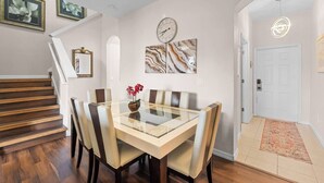 A dining area with a glass table, cushioned chairs, a clock, and abstract art on the wall. - Charming 4/3 Home in Regal Palms Resort (Davenport)