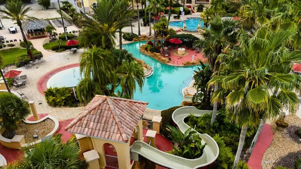 A resort with a central pool, a water slide, and palm trees. - Charming 4/3 Home in Regal Palms Resort (Davenport)