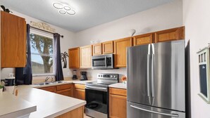 A modern kitchen with wooden cabinets, stainless steel appliances, and a large refrigerator. - Charming 4/3 Home in Regal Palms Resort (Davenport)