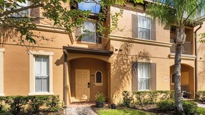 A two-story building with a beige facade, a central entrance with a door, and a small balcony on the upper floor. - Charming 4/3 Home in Regal Palms Resort (Davenport)