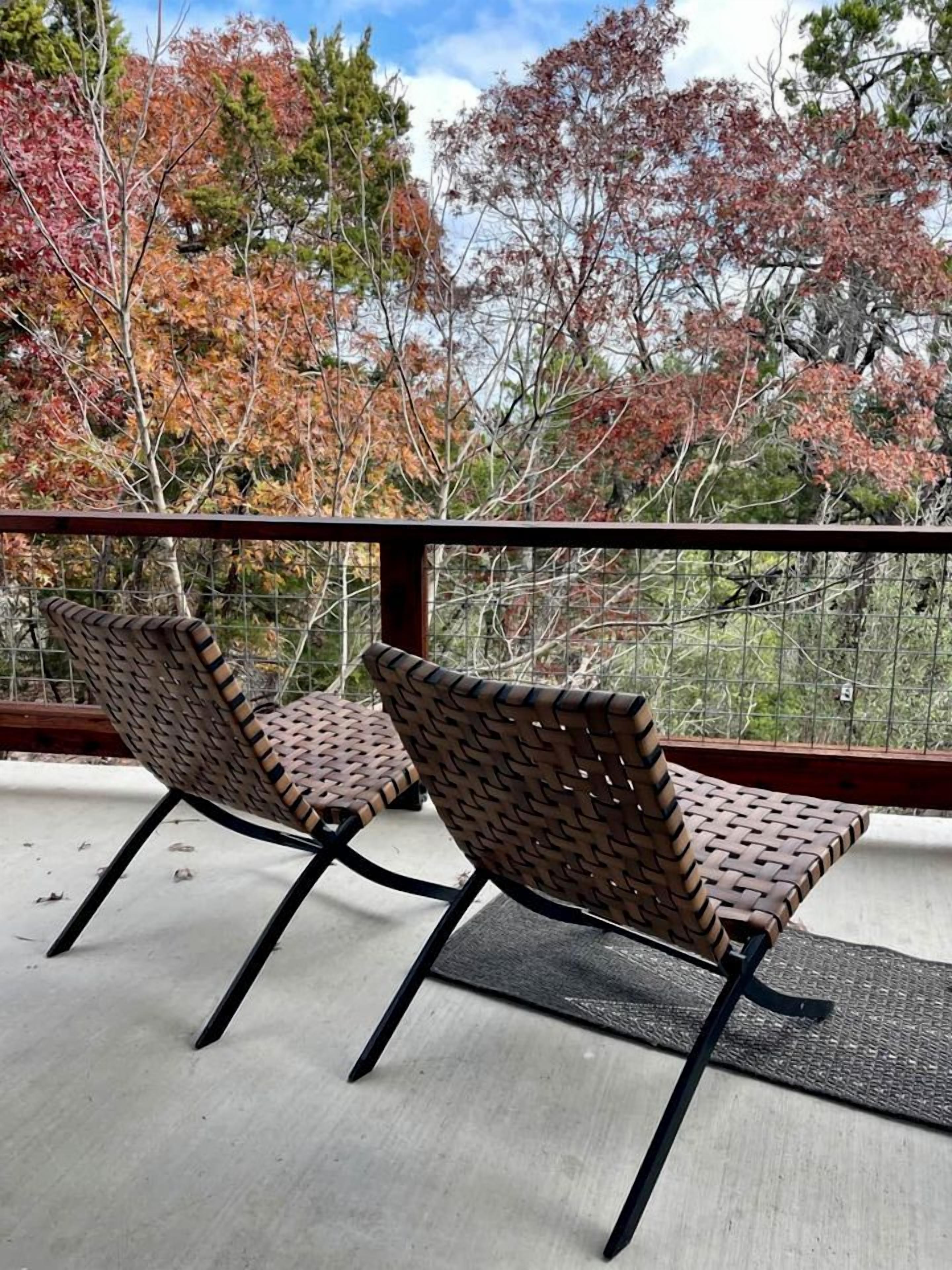 A balcony with two wicker chairs, a metal railing, and a view of autumn trees.