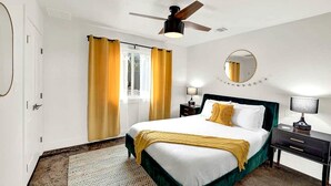 A hotel room with a bed, a ceiling fan, a window with curtains, a bedside table with a lamp, and a round mirror on the wall. - Luxury Cabin for Four for Texas Glamping Retreat (Wimberley)