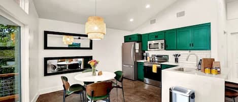 Cocina moderna con armarios verdes, un refrigerador de acero inoxidable y una isla blanca con pileta.