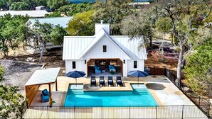 A white house with a pool, outdoor seating, and a view of the surrounding landscape. - Luxury Cabin for Four for Texas Glamping Retreat (Wimberley)