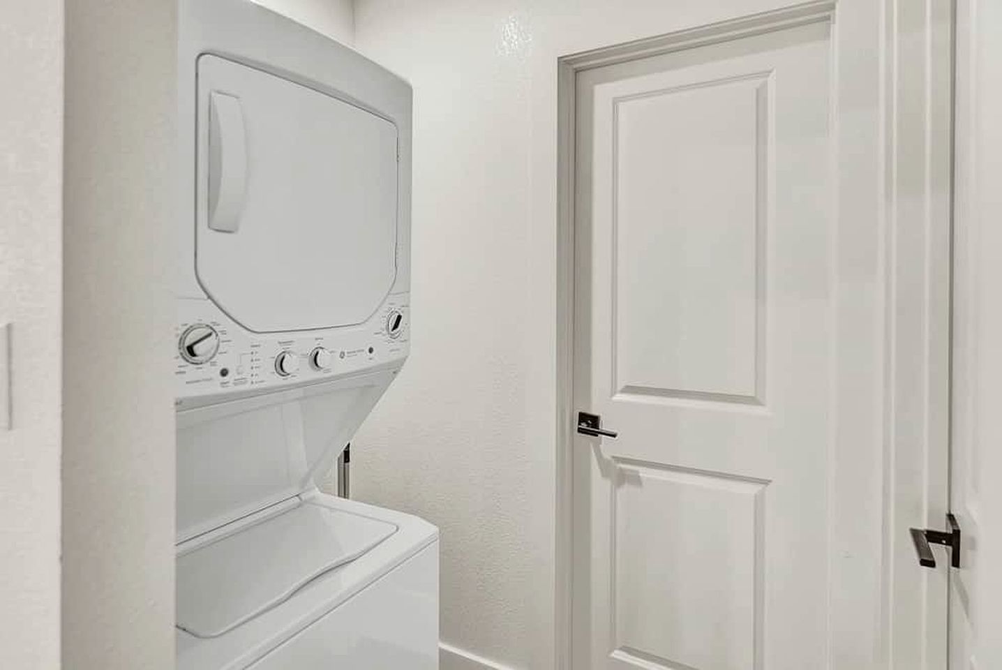 A laundry room with a washing machine and dryer, a white door, and a small shelf.