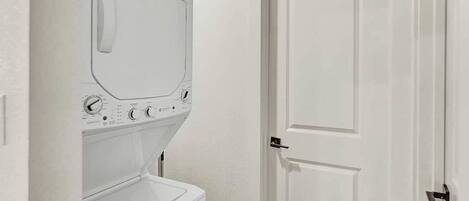 A laundry room with a washing machine and dryer, a white door, and a small shelf.