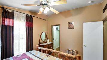 A bedroom with a bed, a wooden bench, a ceiling fan, a mirror, a door, and a white wall.